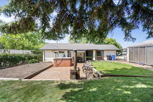 Back of house with a hot tub, a lawn, and a patio