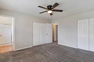 Unfurnished bedroom featuring dark carpet, two closets, ceiling fan, and ensuite bathroom