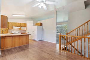 Kitchen with vaulted ceiling, white appliances, light hardwood / wood-style flooring, kitchen peninsula, and ceiling fan