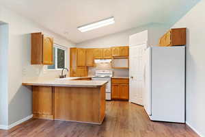 Kitchen with vaulted ceiling, light wood-type flooring, white appliances, sink, and kitchen peninsula