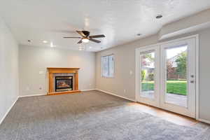 Unfurnished living room with carpet flooring, a textured ceiling, ceiling fan, and a tile fireplace