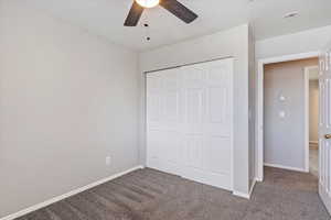 Unfurnished bedroom featuring a textured ceiling, dark carpet, ceiling fan, and a closet