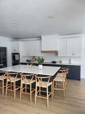 Kitchen with white cabinets, a kitchen breakfast bar, stainless steel double oven, and light hardwood / wood-style flooring