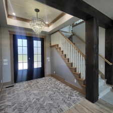 Foyer entrance with a raised ceiling, a chandelier, french doors, and wood-type flooring