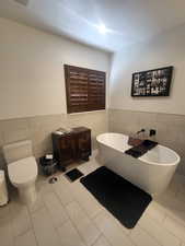 Bathroom with tile walls, toilet, a washtub, and tile patterned flooring