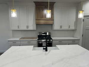 Kitchen with light stone countertops, stainless steel range oven, and hanging light fixtures