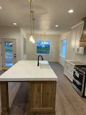 Kitchen with stainless steel range with gas cooktop, sink, an island with sink, white cabinets, and decorative light fixtures