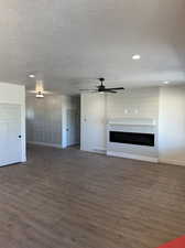 Unfurnished living room featuring ceiling fan, a textured ceiling, and dark hardwood / wood-style flooring