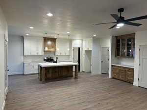 Kitchen featuring white cabinets, pendant lighting, ceiling fan, hardwood / wood-style flooring, and a center island with sink