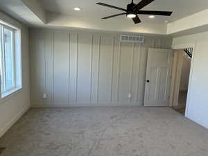 Unfurnished bedroom with a tray ceiling, multiple windows, light colored carpet, and ceiling fan