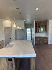 Kitchen with light stone counters, a textured ceiling, hanging light fixtures, and dark wood-type flooring