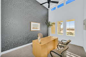 Carpeted office space featuring ceiling fan and a high ceiling