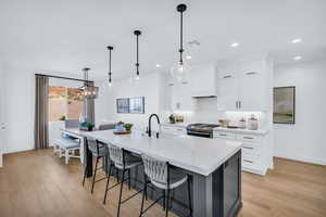 Kitchen featuring light hardwood / wood-style floors, an island with sink, white cabinets, gas range, and decorative light fixtures