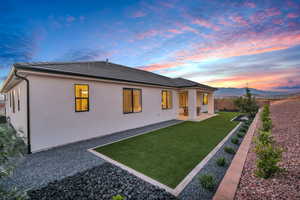 Back house at dusk with a yard, a mountain view, and a patio area