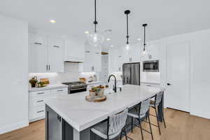 Kitchen featuring light hardwood / wood-style flooring, white cabinetry, appliances with stainless steel finishes, and a kitchen island with sink