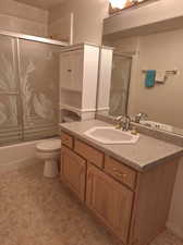 Full bathroom with combined bath / shower with glass door, vanity, and toilet