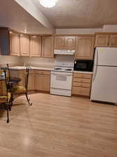 Kitchen with a textured ceiling, white appliances, light wood-type flooring, and light brown cabinetry