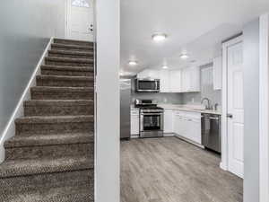 Kitchen with light hardwood / wood-style floors, sink, stainless steel appliances, and white cabinets