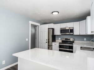 Kitchen with stainless steel appliances, white cabinetry, a textured ceiling, and sink