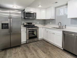 Kitchen featuring appliances with stainless steel finishes, dark wood-type flooring, white cabinets, a textured ceiling, and sink