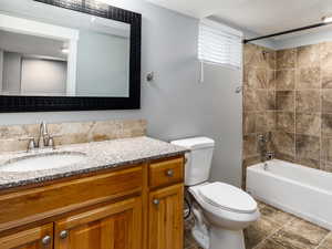 Full bathroom featuring vanity, tiled shower / bath combo, toilet, and tile patterned flooring