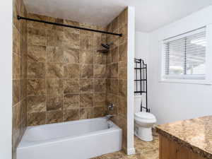 Full bathroom with a textured ceiling, tiled shower / bath, vanity, and toilet