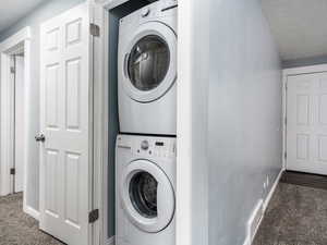 Clothes washing area with dark carpet, a textured ceiling, and stacked washer and dryer