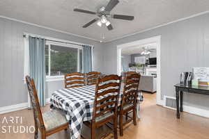 Dining area with light hardwood / wood-style flooring, wooden walls, ceiling fan, and a textured ceiling