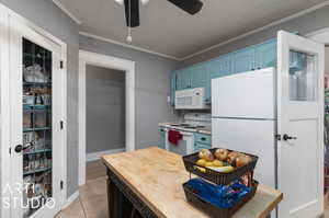 Kitchen featuring white appliances, light tile patterned floors, blue cabinetry, crown molding, and ceiling fan