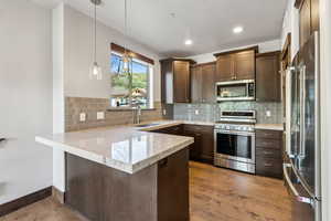 Kitchen with hanging light fixtures, stainless steel appliances, dark wood-type flooring, and kitchen peninsula