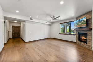 Unfurnished living room with light wood-type flooring, ceiling fan, and a stone fireplace