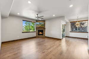 Unfurnished living room featuring ceiling fan with notable chandelier, a stone fireplace, wood-type flooring, and a wealth of natural light