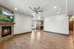 Unfurnished living room featuring light wood-type flooring, ceiling fan, and a stone fireplace