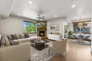 Living room with wood-type flooring, ceiling fan with notable chandelier, a fireplace, and a wealth of natural light