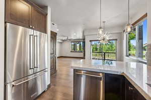 Kitchen with pendant lighting, wood-type flooring, dark brown cabinets, appliances with stainless steel finishes, and light stone countertops