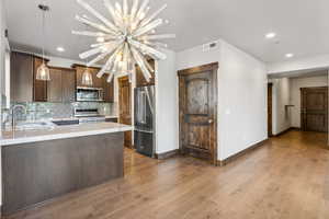 Kitchen with light wood-type flooring, a chandelier, sink, backsplash, and appliances with stainless steel finishes