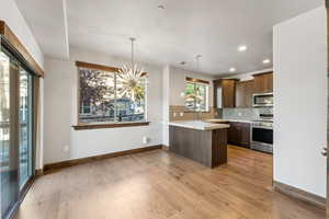 Kitchen featuring pendant lighting, kitchen peninsula, tasteful backsplash, light hardwood / wood-style flooring, and appliances with stainless steel finishes