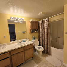 Full bathroom featuring a textured ceiling, vanity, toilet, and shower / bath combo with shower curtain