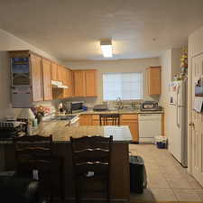 Kitchen with appliances with stainless steel finishes, kitchen peninsula, light tile patterned floors, a textured ceiling, and sink