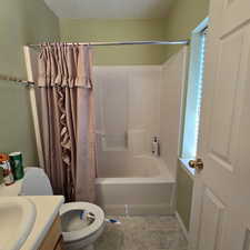 Full bathroom with vanity, a textured ceiling, shower / bath combo with shower curtain, tile patterned floors, and toilet