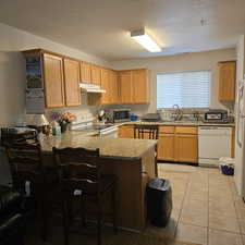 Kitchen with white appliances, kitchen peninsula, light stone countertops, a textured ceiling, and sink