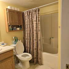 Full bathroom featuring shower / bath combo, a textured ceiling, vanity, and toilet