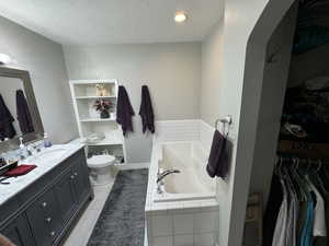 Bathroom with tile patterned flooring, a textured ceiling, tiled tub, vanity, and toilet