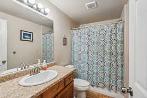 Full bathroom featuring toilet, shower / tub combo with curtain, a textured ceiling, and vanity