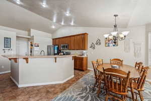 Kitchen featuring appliances with stainless steel finishes, an island with sink, a breakfast bar, a chandelier, and lofted ceiling