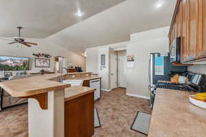 Kitchen featuring vaulted ceiling, stainless steel appliances, sink, ceiling fan, and a kitchen bar