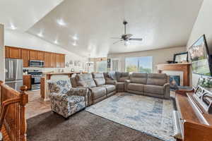 Carpeted living room featuring vaulted ceiling, ceiling fan with notable chandelier, and a tile fireplace