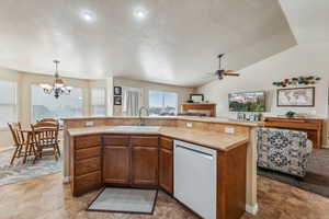 Kitchen featuring ceiling fan with notable chandelier, white dishwasher, sink, and a center island with sink