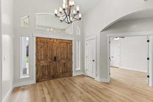 Foyer entrance with ceiling fan with notable chandelier, a high ceiling, and light hardwood / wood-style floors