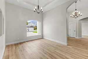 Music/Formal Dining  Unfurnished room featuring crown molding, a tray ceiling, an inviting chandelier, and light hardwood / wood-style flooring